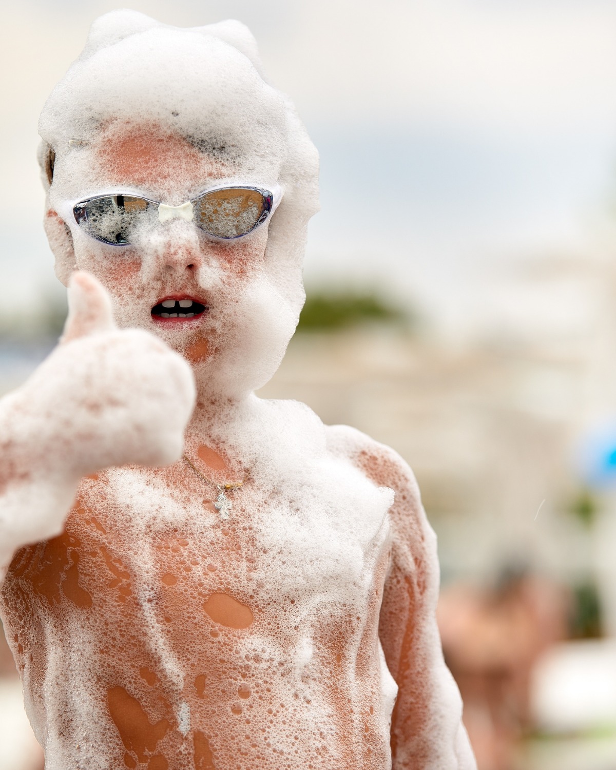 Boy in swim goggles covered in foam giving a thumbs up