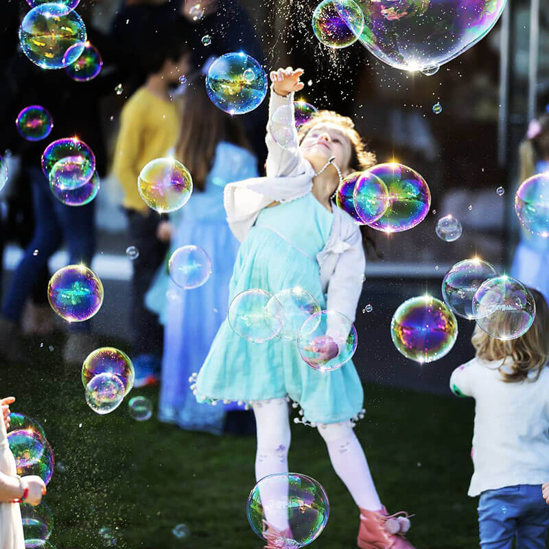 Little girl in a princess dress reaching for giant bubbles