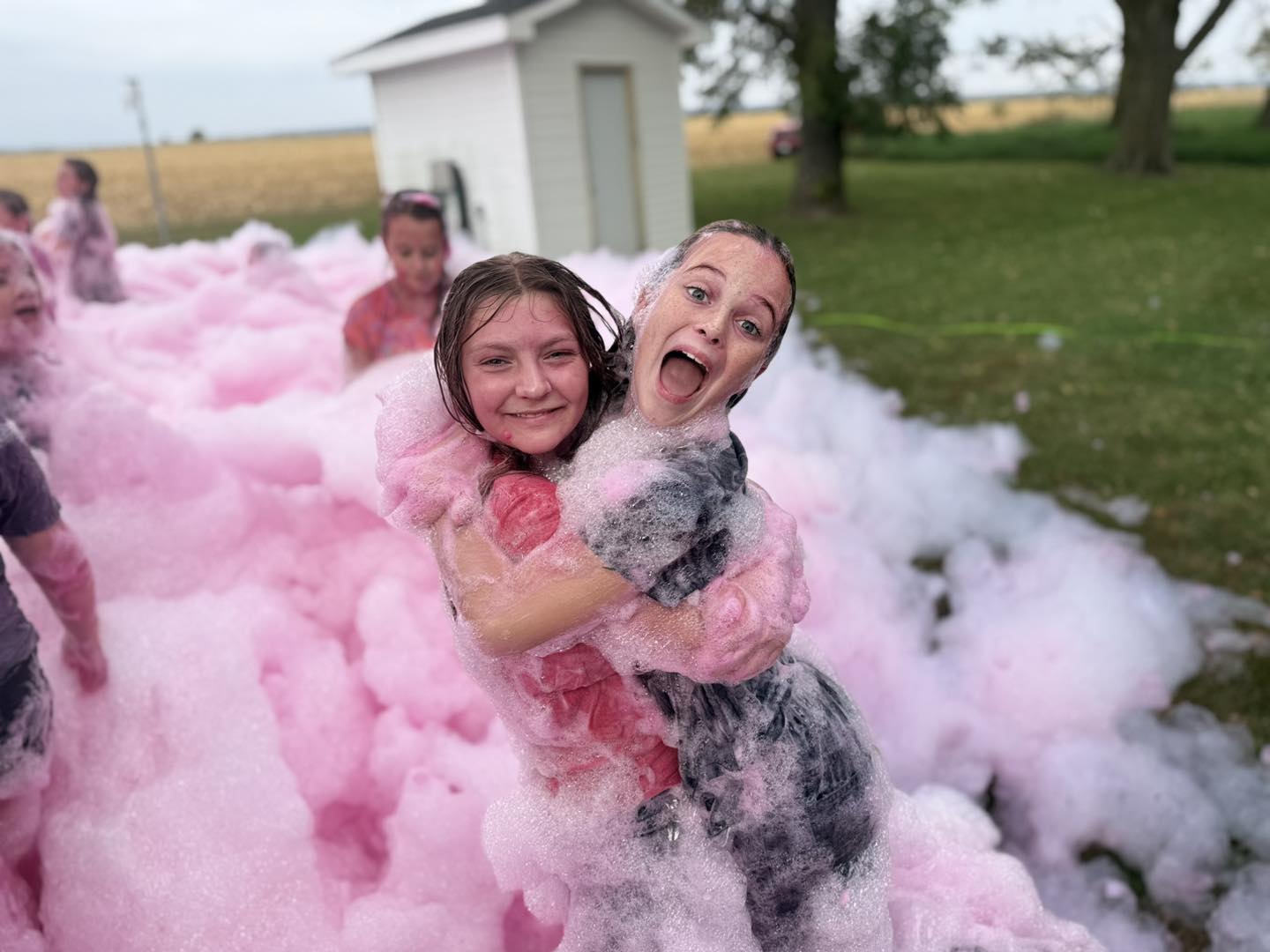 Two girls hugging and laughing in pink foam