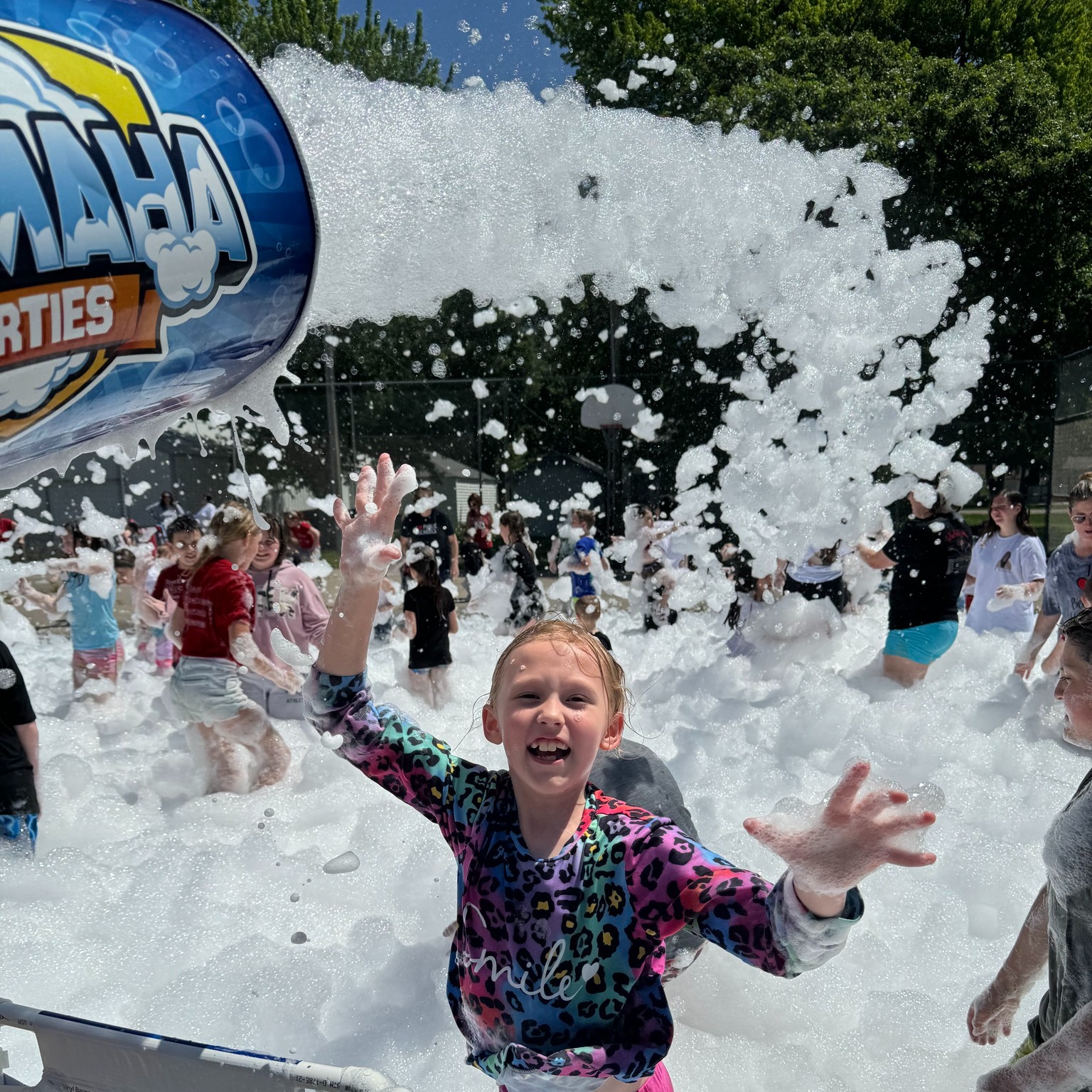 Girl cheering with arms raised as foam pours overhead at a Foamaha event